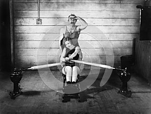 Woman sitting on a rowing machine with a man behind her