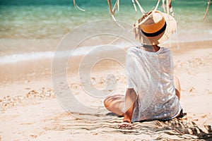 Woman sitting on the sea beach in palm tree shadow. Safety tanning concept