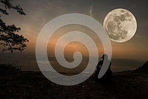 Woman sitting serenely of the cliff and looking at the valley and mountains with moon