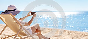 Woman sitting with smartphone in the chaise lounge on the sea beach.