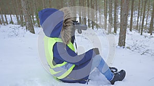 Woman sitting on snow looking through binoculars in forest