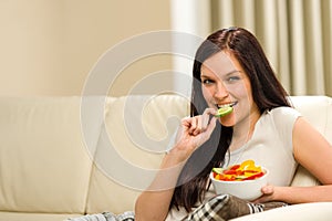 Woman sitting on sofa eating mixed salad