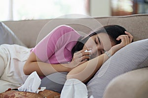 Woman sitting on sofa feeling bad blowing nose sneezing sick