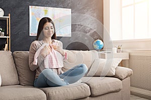 Woman sitting on the sofa holding baby t-shirt indoors