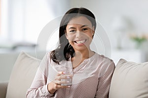 Woman sitting on sofa holding glass of water feels healthy