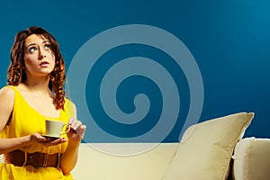 Woman sitting on sofa holds coffee cup