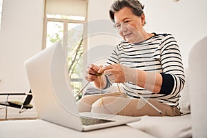 Woman sitting on sofa and knitting with a wool at the retirement house