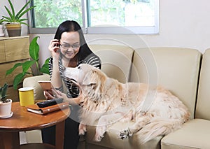 Woman sitting on sofa in living room, listen to the music from mobile phone and looking at her golden retriever dog who`s trying