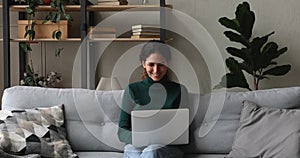 Woman sitting on sofa in living room texting on laptop