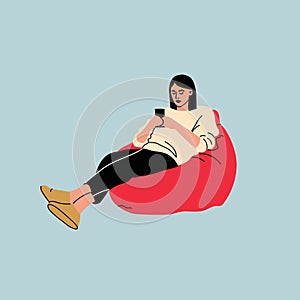 Woman sitting on sofa pouf holds smartphone in her hand. Casual lady and browsing social media on mobile device. Girl on