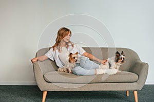 Woman is sitting on a sofa with two cute dogs
