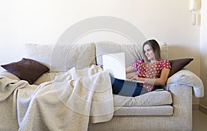 Woman sitting on the sofa while watching a laptop and online learning and teleworking from home. Boredom