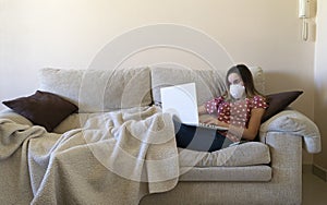 Woman sitting on the sofa while watching a laptop and online learning and teleworking from home with a ppe mask.Quarantine