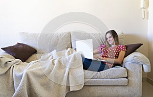 Woman sitting on the sofa while watching a laptop and online learning and teleworking from home while smiling