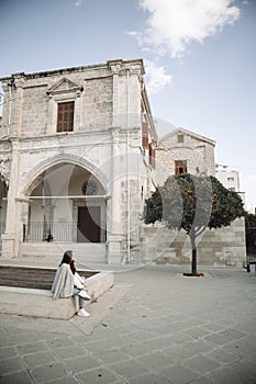 Woman is sitting at the square with ancient building and tangerine tree