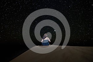A woman sitting staring at the starry sky towards Venus, on a dune in the Erg Chebbi desert