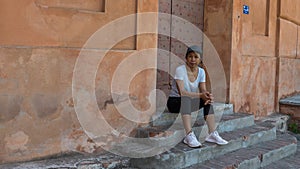 Woman sitting on steps in front of doorway with cap and sneakers