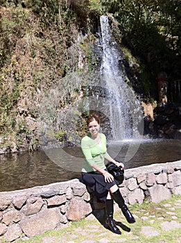 woman sitting on a stone wall, near a waterfall