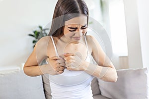 Woman sitting with strong chest pain and hands touching her chest while having trouble at home, Heart attack or heart failure