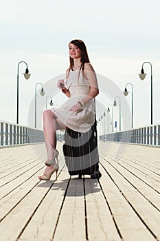 Woman sitting on suitcase, pier in background