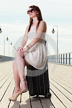 Woman sitting on suitcase, pier in background