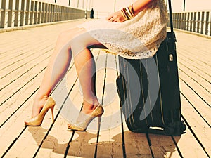 Woman sitting on suitcase, pier in background