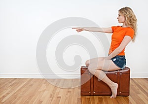 Woman sitting on a suitcase and pointing direction