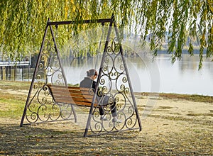 Woman is sitting on a swing. Lonely middle-aged woman on a swing.