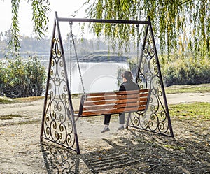 Woman is sitting on a swing. Lonely middle-aged woman on a swing.