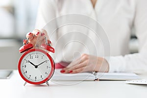 Woman sitting at table with book and clicking on alarm clock closeup