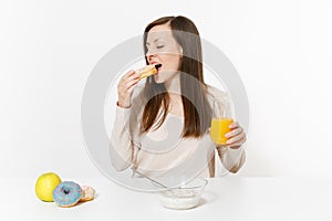 Woman sitting at table breakfast with cereals and milk, orange juice in glass, biting donut isolated on white background