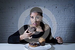 Woman sitting at table feeling guilty forgetting diet eating dish full of junk sugary unhealthy food