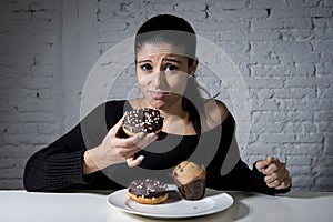 Woman sitting at table feeling guilty forgetting diet eating dish full of junk sugary unhealthy food