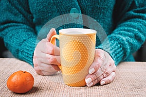 Woman sitting at the table and holding a cup of tea in her hands