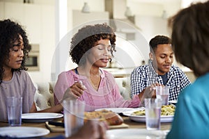 Woman sitting at the table holding hands with her young adult children saying grace before dinner