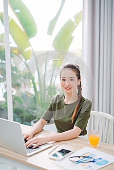 Woman sitting at the table at home working using computer laptop with a happy face standing and smiling with a confident smile
