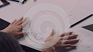 Woman sitting at the table in office, holding pencil and drawing sketch of shoes on paper.