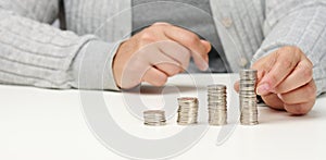 Woman is sitting at the table and a stack of coins on the table. Calculation of expenses and income, subsidy, tax