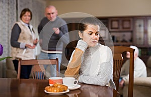 Woman sitting at table, unhappy family quarrelling on backgroud