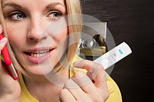 Woman is sitting on the toilet and holding a positive pregnancy test and mobile phone