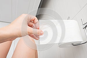 Woman sitting on a toilet in a restroom and rips off a piece of toilet paper from a roll, digestive problems and defecation