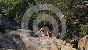 Woman sitting on top of hill looks at panoramic view of mountain range sunrise. Lady is dangerously