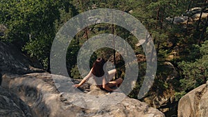 Woman sitting on top of hill looks at panoramic view of mountain range sunrise. Lady is dangerously