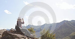 Woman sitting on top of mounting admiring amazing view on valley, hills, river.