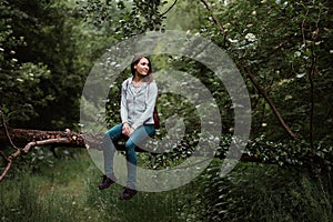 Woman sitting on tree branch in deep forest enjoying nature