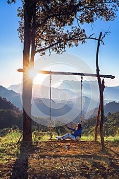 Woman sitting on a tree swing on peaceful morning with sun flare. Lady sitting on a wooden swing at Hadubi viewpoint at the
