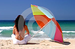 Woman sitting under colorful parasol on white sandy beach