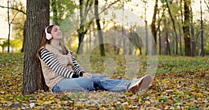 Woman sitting under a tree in autumn park with fallen leaves