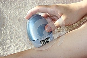 A woman sitting using a depilatory depilator. Smooth legs. Female epilating epilator for hair electric , belonging to the