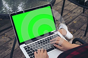 A woman sitting , using and typing on laptop with blank green screen on thigh at outdoor background